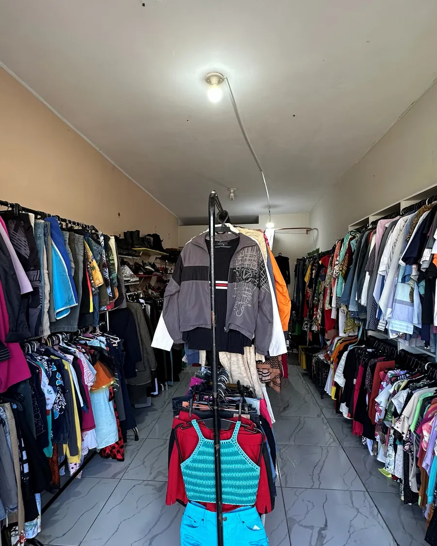 Corredor da loja com araras cheias de roupa dos dois lados